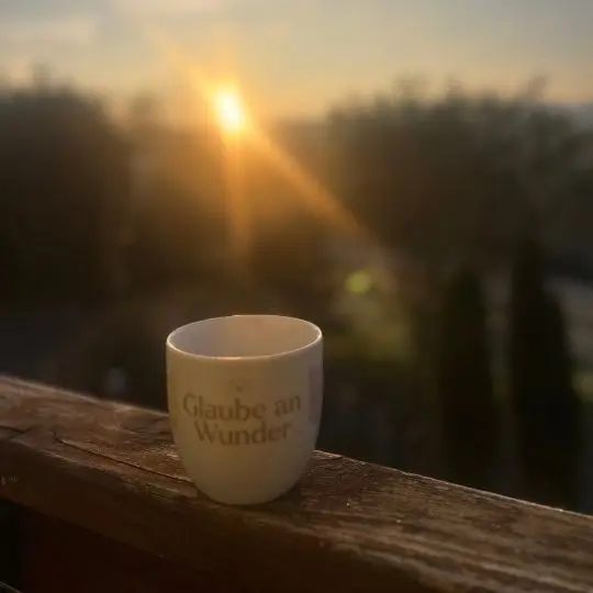 Tasse mit dem Schriftzug „Glaube an Wunder“ vor dem Sonnenaufgang